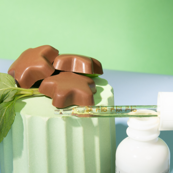 Three star-shaped chocolate-covered chews on a mint-green pedestal next to a glass dropper and white bottle